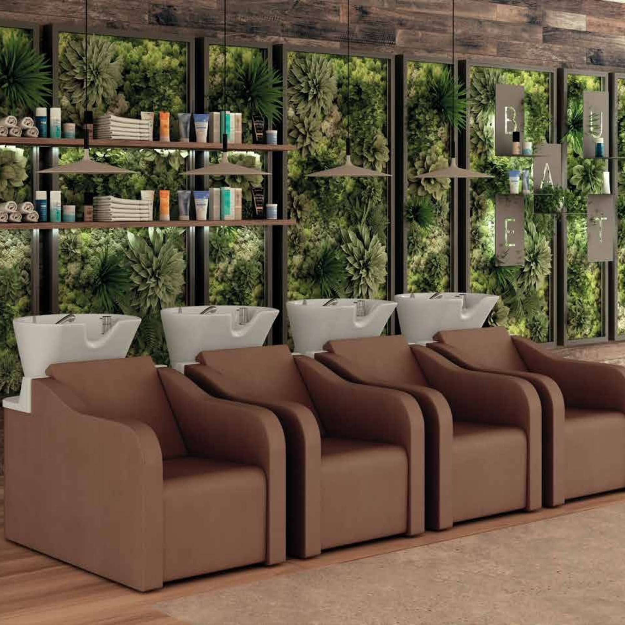 frizerski salon s četiri smeđa glavopera, bijelim umivaonicima i zidom prekrivenim zelenim biljkama s drvenim policama i visećim rasvjetom